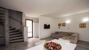 Una sala de estar moderna con una escalera, un televisor de pantalla plana y un comedor con un tazón de comida.
