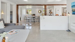 A spacious living area with a sofa, a coffee table, and a dining area with chairs and a table. There is a kitchen visible in the background.