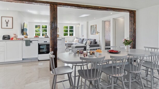 A modern kitchen with white cabinetry, a dining area with grey chairs and a round table, and a living room with a grey sofa and a coffee table.