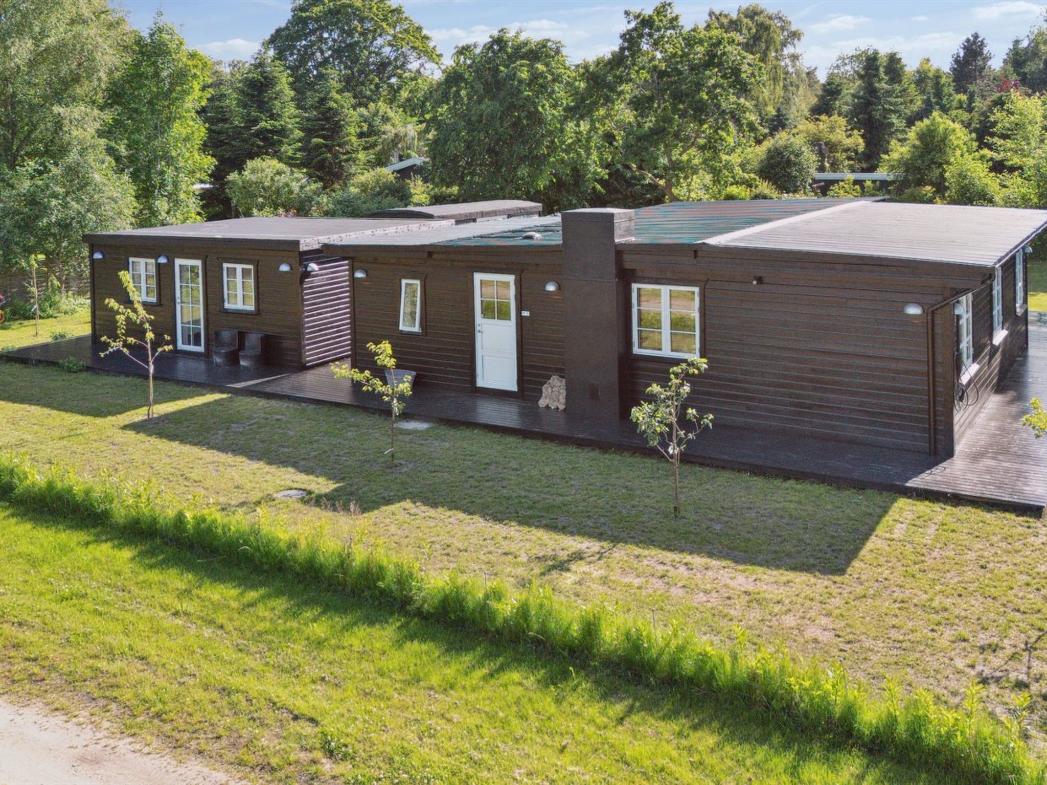 Een modern gebouw met twee verdiepingen, een plat dak, een overdekte patio en een kleine tuin met jonge bomen.