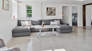 A modern living room with a grey sectional sofa, a white coffee table, and a large window with a view of greenery.