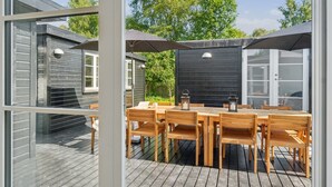 A wooden deck with a dining table and chairs, surrounded by umbrellas, and a view of a house with a black exterior wall.