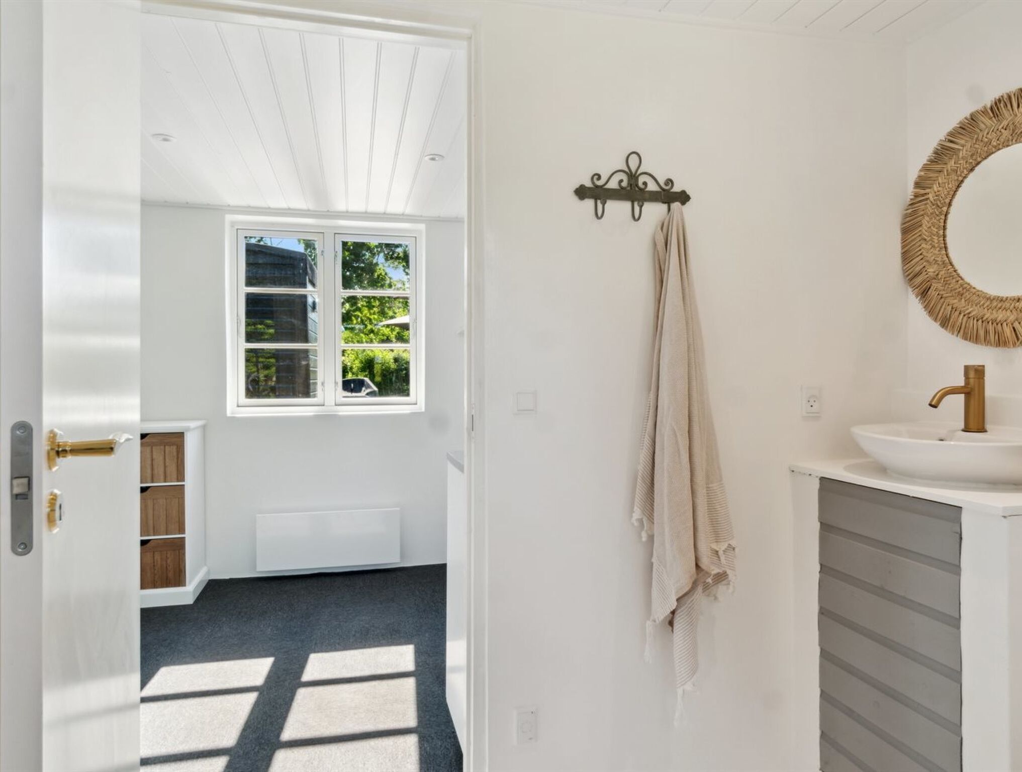 Une salle de bain avec un lavabo blanc, un miroir rond doté d’un cadre tressé et une serviette suspendue à un porte-serviettes.