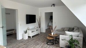 A modern living room with a flat-screen TV, a white sofa, a small round table, and a bench.