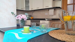 A kitchen with white cabinets, a black countertop, a vase with pink flowers, and a table with a blue tablecloth.