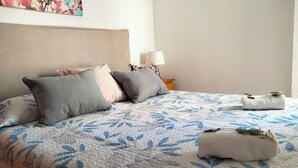 A neatly made bed with a floral-patterned bedspread, two pillows, and two rolled towels with lavender on a white headboard.