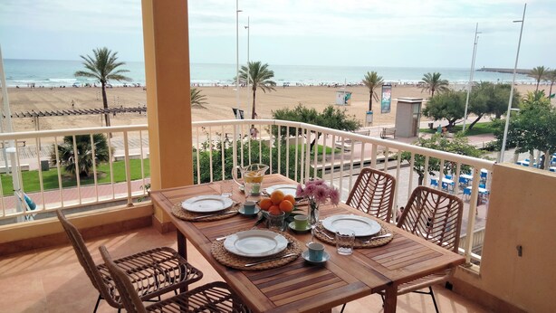 A balcony with a wooden table set for two, overlooking a beach.