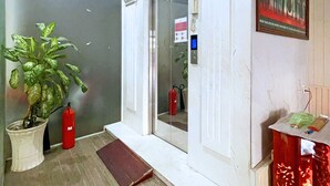 Un pasillo con una planta en maceta, un extintor y una puerta que da a otra habitación.