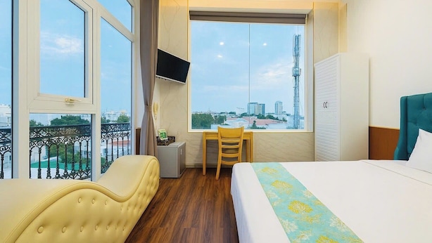 Habitación de hotel con cama, escritorio, silla, televisor y balcón con vistas a la ciudad.