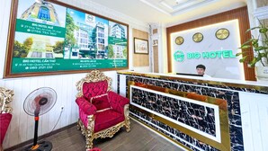Zona de recepción de hotel con un sillón rojo, un mostrador de mármol y un anuncio enmarcado de la propiedad en la pared.