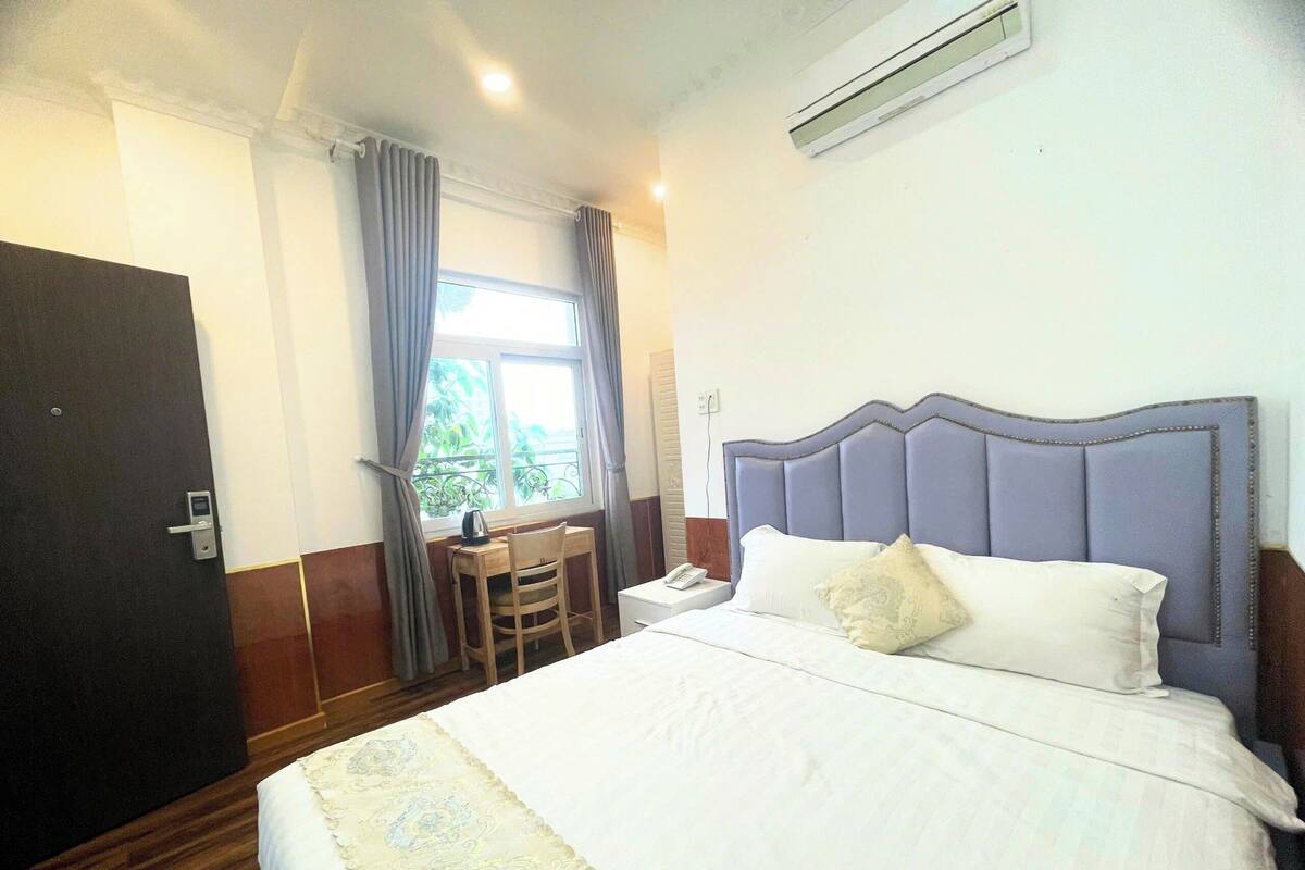 Une chambre d’hôtel avec un grand lit, un bureau avec une chaise, une fenêtre avec des rideaux et un climatiseur fixé au mur.