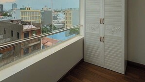 Una habitación con un ventanal grande, suelo de madera y un armario blanco con tiradores decorativos.