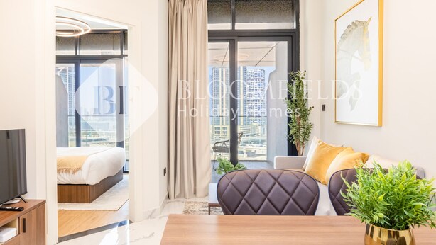 Una habitación de hotel moderna con cama, sofá, televisión y un amplio ventanal con vista a la ciudad.