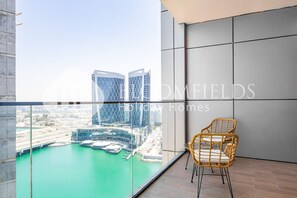 A balcony with a view of a marina and buildings, a wicker chair, and a glass partition.
