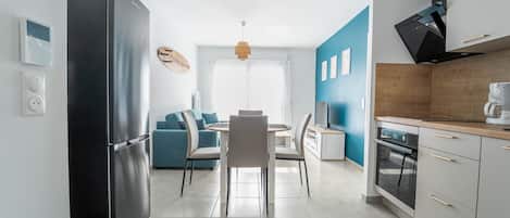 Cozinha moderna com geladeira preta, área de jantar com sofá azul e bancada de madeira com cafeteira.
