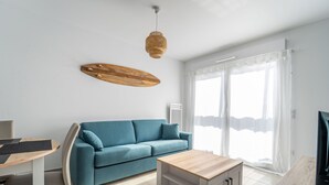 Una sala moderna con un sofá azul, una mesa de centro de madera y una zona de comedor con una mesa y sillas blancas.