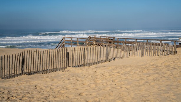 Una playa arenosa con una valla de madera y una estructura al fondo.
