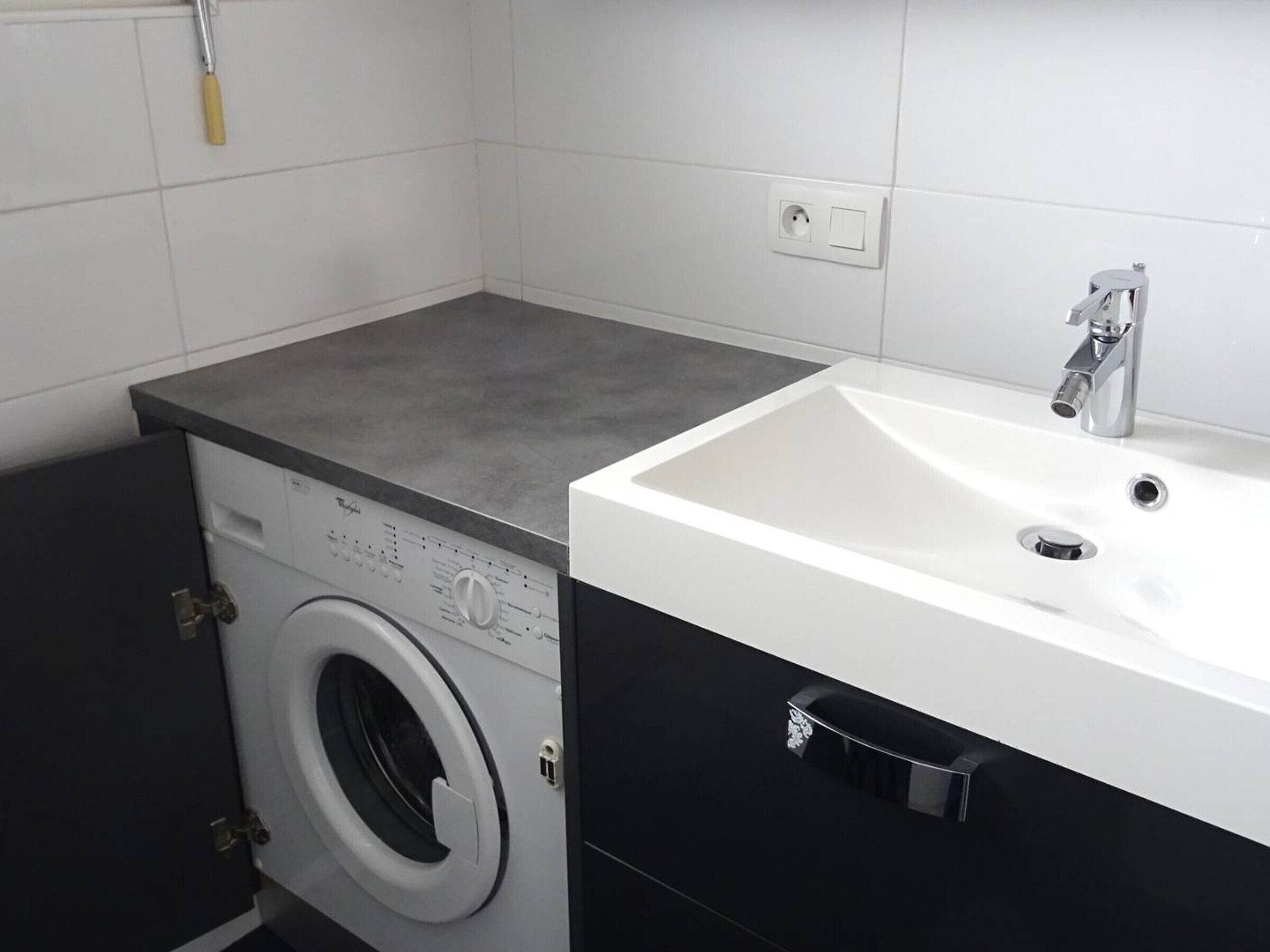 A compact laundry room with a washing machine, a sink, and a towel rack.