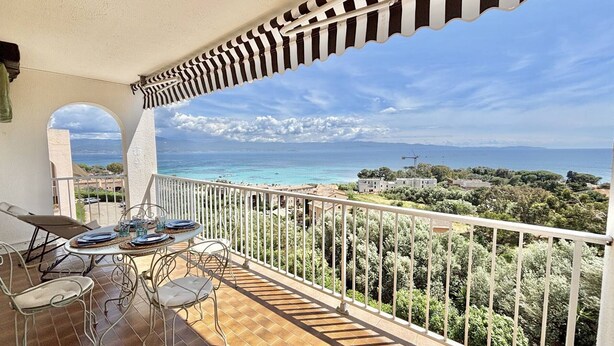 Un balcon avec vue sur la mer, une table avec des chaises et un auvent à rayures.