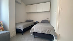A small, clean room with two single beds, a small table, and a chair. - Cozy apartment near the Thermal Baths in Balaruc-les-Bains (Balaruc-les-Bains)