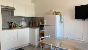 A modern kitchen with white cabinets, a microwave, a toaster, and a refrigerator. There is a dining table with chairs and a TV mounted on the wall. - Cozy apartment near the Thermal Baths in Balaruc-les-Bains (Balaruc-les-Bains)