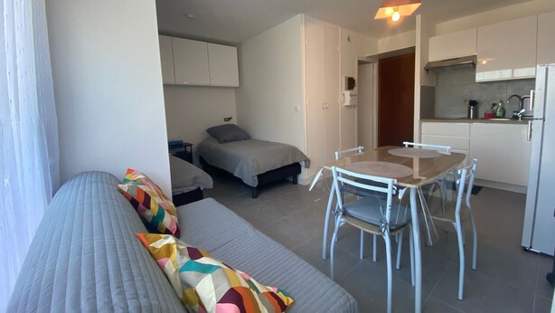 A compact living space with a sofa, a small dining table with chairs, a kitchenette, and a bed. - Cozy apartment near the Thermal Baths in Balaruc-les-Bains (Balaruc-les-Bains)