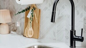 A kitchen with a double stainless steel sink, a black faucet, a wooden cutting board with a roll of paper towels, and a lamp. - Chic 2BR/2BA Stay | Downtown & Capitol Views (Montgomery)
