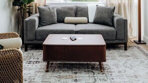 A modern living room with a grey sofa, a wooden coffee table, and a large window with curtains. - Chic 2BR/2BA Stay | Downtown & Capitol Views (Montgomery)