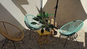A patio with two wicker chairs, a small table with a potted plant, and a large umbrella.