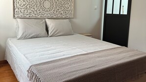 A neatly made bed with a patterned bedspread and pillows, a decorative wall panel, and a window with blinds.