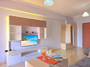 A modern living room with a flat-screen TV mounted on the wall, a coffee table with drinks, and a magazine. - Mandalay Suites by the Beach 079 (Durres)