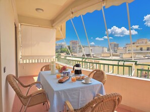 A balcony with a table set for breakfast, wicker chairs, and a view of buildings. - Mandalay Suites by the Beach 079 (Durres)