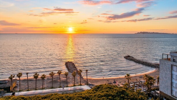 A coastal sunset view with a rocky breakwater, palm trees, and a beach. - Modern Apartment a Short Walk from the Beach (Durres)