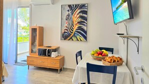 A modern room with a dining table, a fruit bowl, a painting, and a TV on the wall. - Modern Apartment a Short Walk from the Beach (Durres)