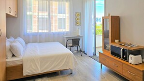 A hotel room with a bed, a desk, a microwave, and a view of the outside. - Modern Apartment a Short Walk from the Beach (Durres)