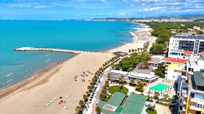 A coastal hotel with a beach view, a swimming pool, and a parking area.