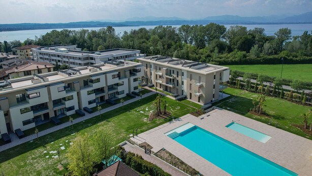 Ein modernes Mehrstöckiges Hotel mit Swimmingpool, umgeben von Grünflächen und Seeblick.