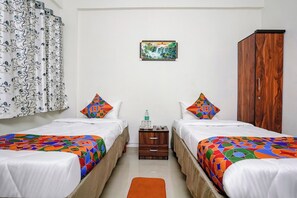 A hotel room with two beds, a wooden wardrobe, a small table with a bottle, and a painting on the wall. - Hotel Comfort Caves (Nashik)