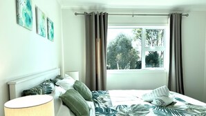 A neatly made bed with a tropical leaf-patterned bedspread, a bedside lamp, and a window with curtains. - Newly Built 3 BDMs Besides Chartwell Shopping Mall (Hamilton)