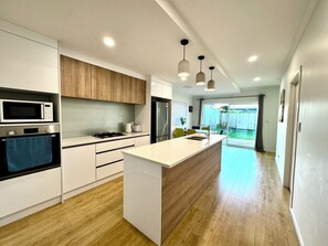 Une cuisine moderne dotée d’un îlot central, d’appareils électroménagers intégrés et de luminaires suspendus.