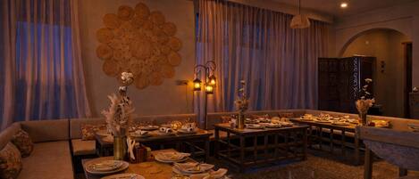 A dining area with round tables set for a meal, a sofa, and a decorative wall.