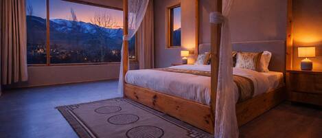 A four-poster bed with a view of mountains through the window.