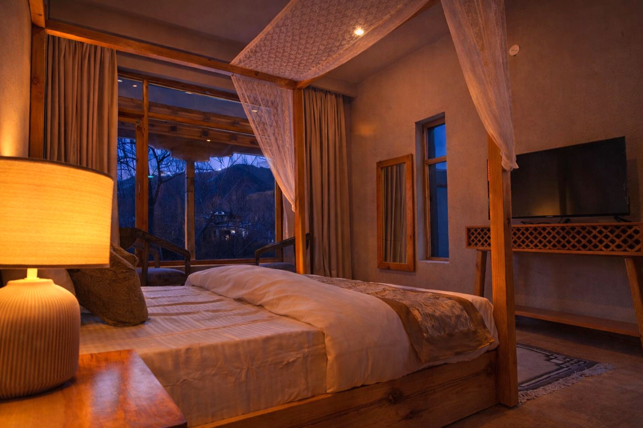 A bedroom with a bed, a TV, a lamp, and a view of the outdoors.
