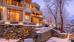 A multi-story building with stone steps leading to a wooden balcony, surrounded by snow. - The Vintage Villas Resort Ladakh - Luxury Stay with Mountain Views (Leh)