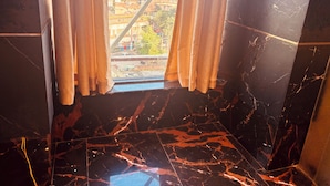 A room with a view through a window with curtains, featuring a marble floor and a metal-framed window structure.