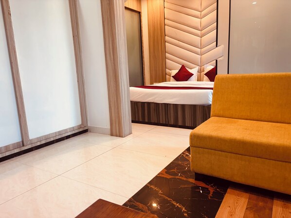 A modern hotel room with a bed, a yellow armchair, and a wooden floor. - Hotel Chariot Inn (Deoghar)
