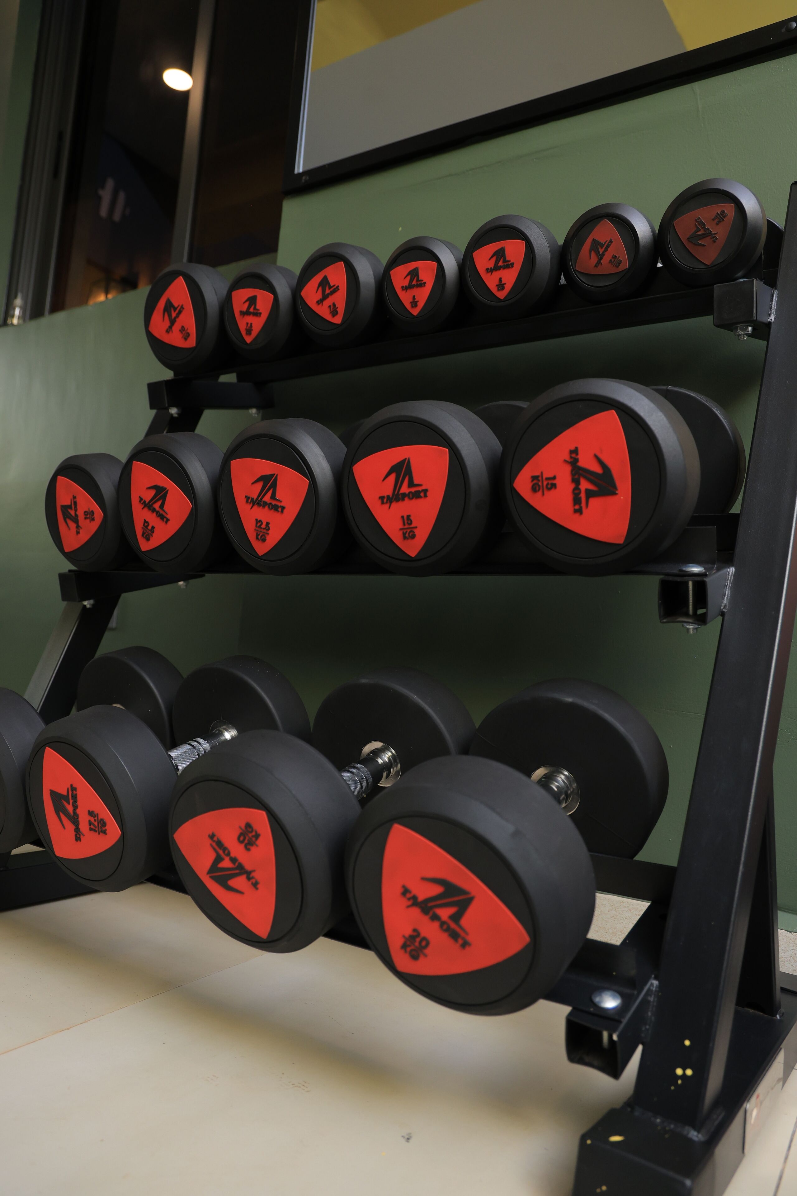 A rack of dumbbells with red and black labels, arranged on a black stand.