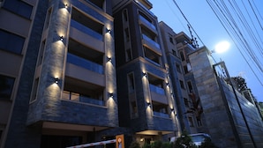 A multi-story building with illuminated exterior lights, a gated entrance, and a clear sky. - Abrish Hotel and Apartment (Kampala)