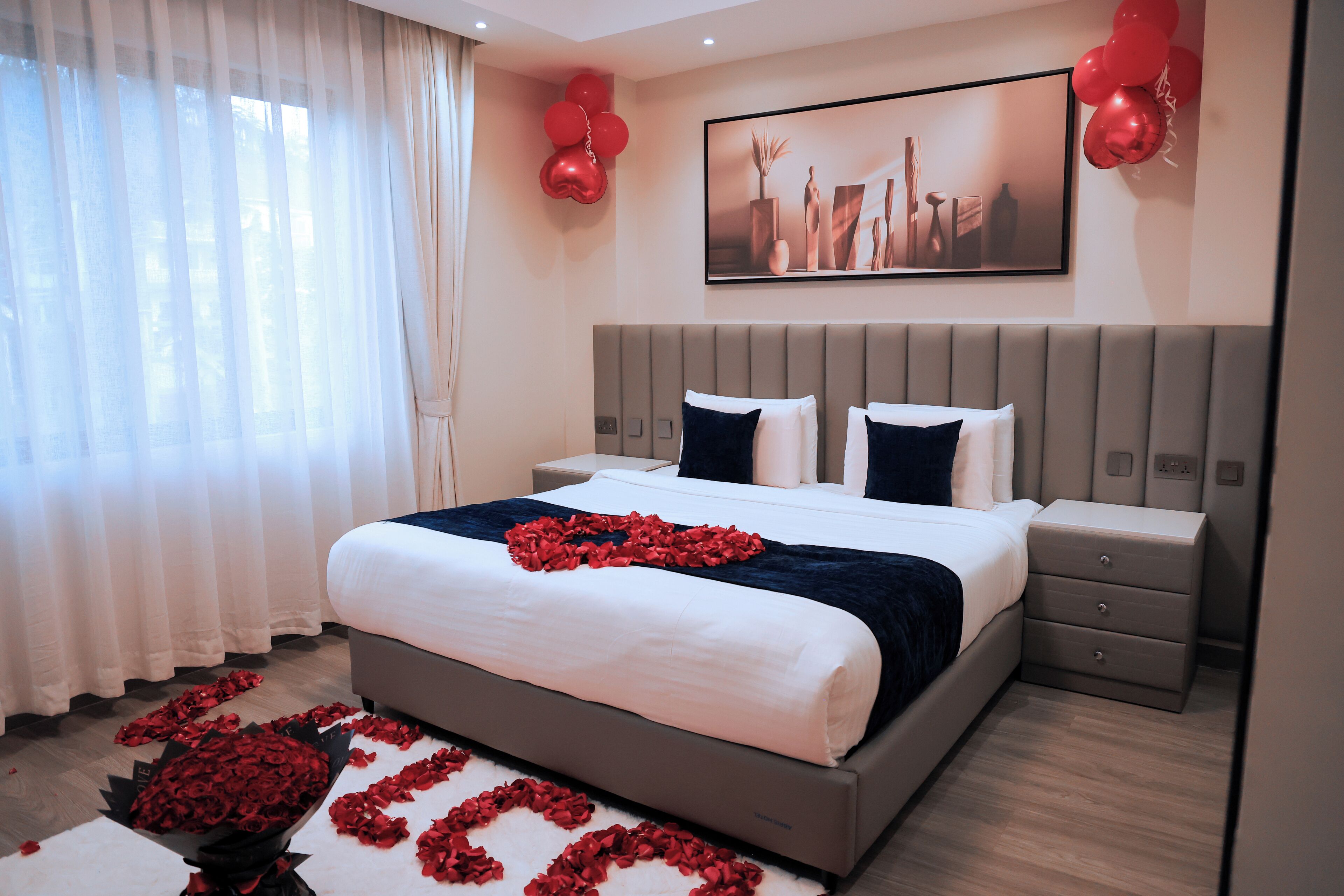 A modern bedroom with a large bed, bedside tables, and a decorative arrangement of red roses on the floor.