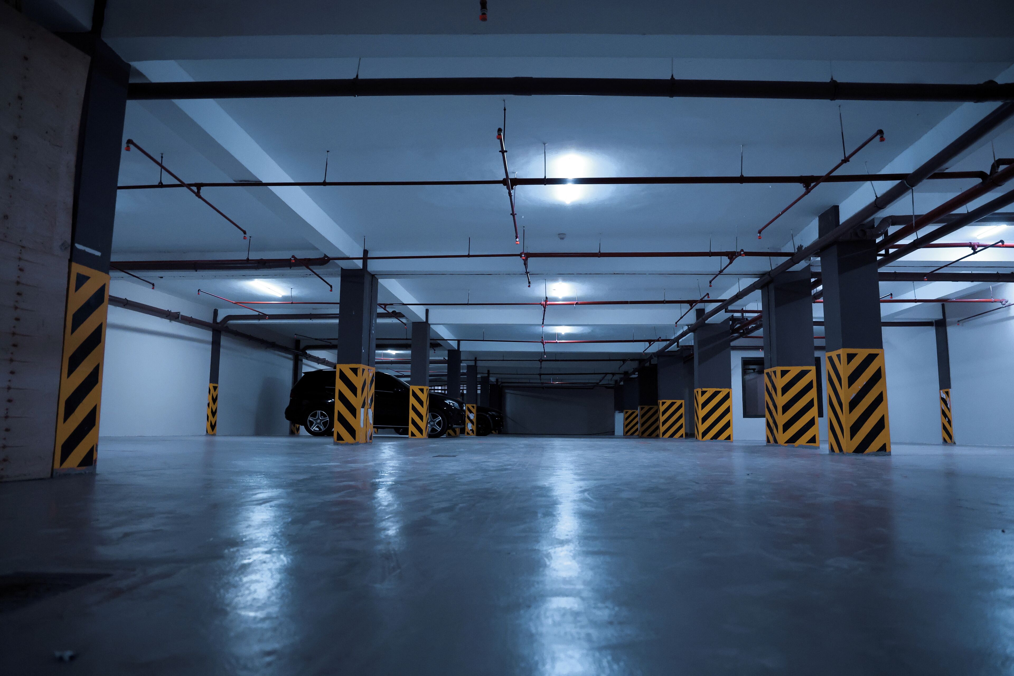 Un parking à plusieurs niveaux, doté de planchers en béton, de barrières rayées de jaune et de noir, et de poutres apparentes.